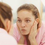 woman looking in mirror with hands on cheecks