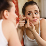 Woman looking in mirror and squeezing pimple