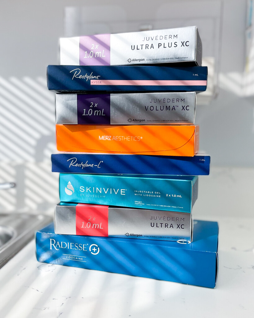 Stack of dermal fillers available at Simply Dermatology. Juvederm, Restylane, Radiesse, and Skinvive filler boxes stacked on each other. Prejuvenation treatments at Simply Dermatology.