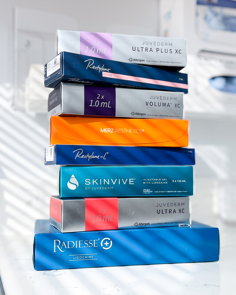 Stack of Juvederm, Restylane, Radiesse, and Skinvive filler boxes used in Botox and filler prejuvenation treatments at Simply Dermatology.