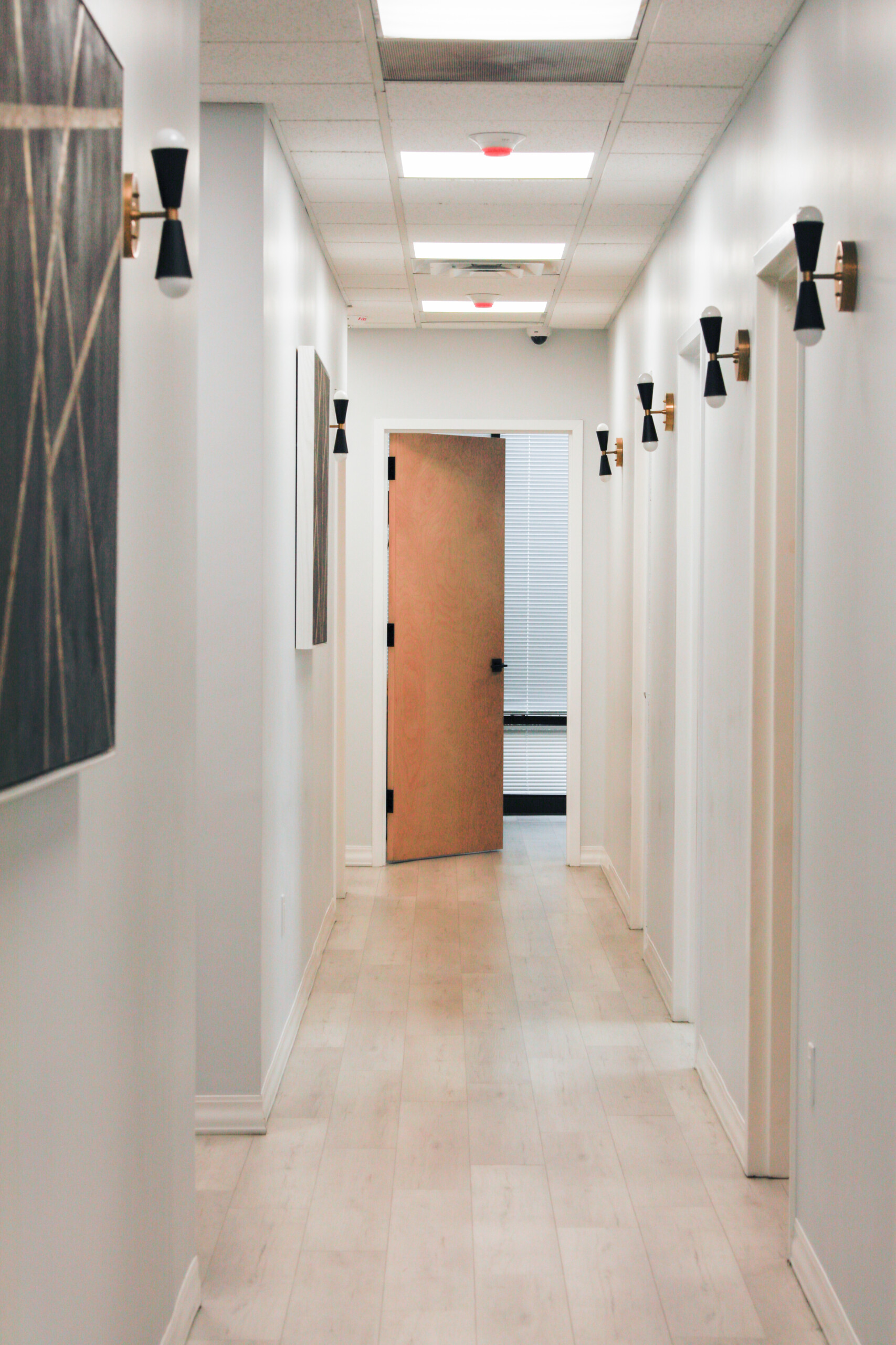 A bright hallway inside Simply Dermatology featuring treatment room doors and modern wall lighting, creating a calm clinical environment.