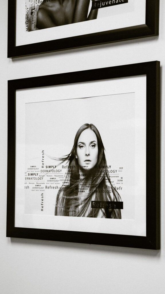 A framed black-and-white portrait of a woman displayed on the clinic wall at Simply Derm, featuring subtle text overlays with the Simply Dermatology branding.