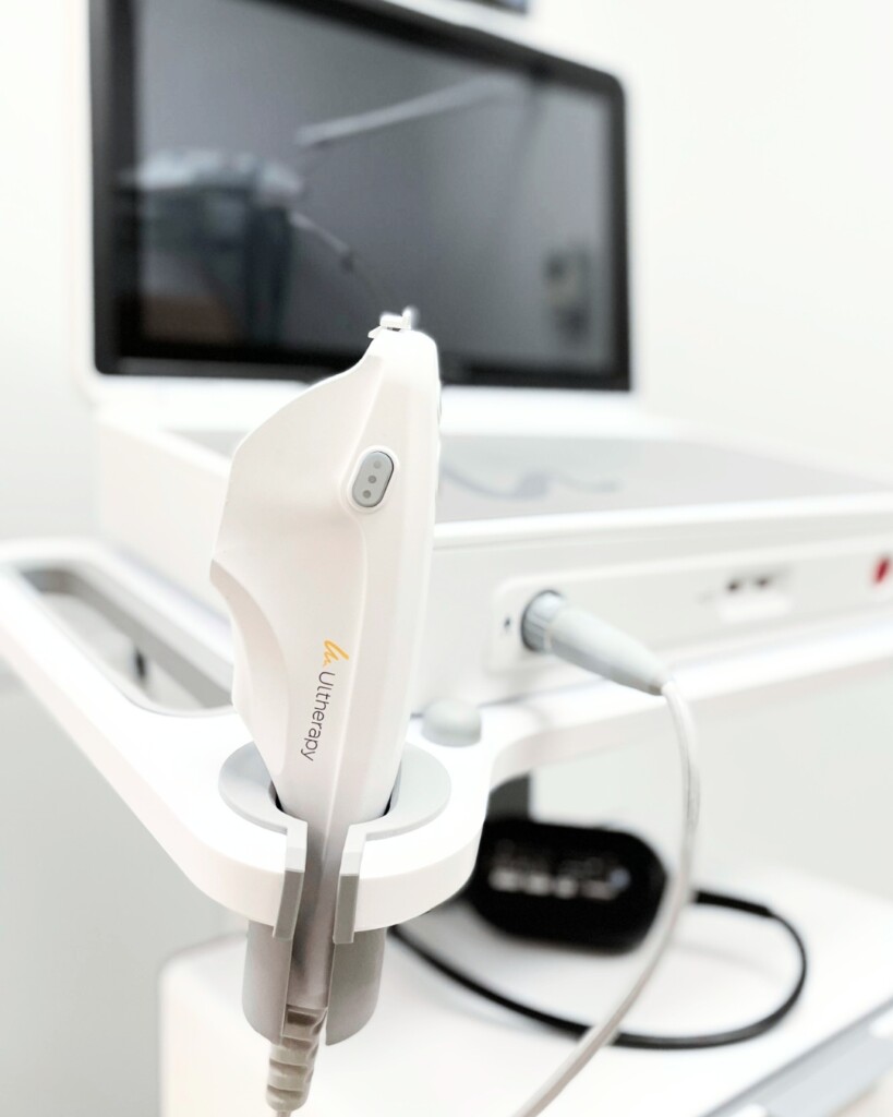 Close-up of an Ultherapy handpiece resting in its holder, with the Ultherapy logo visible and the treatment console behind it.