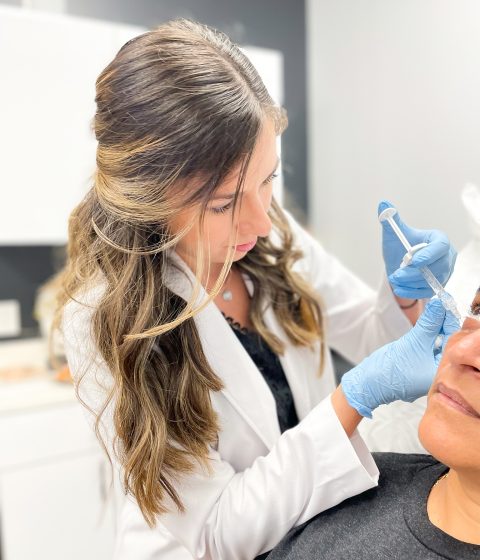 Angela Cusumano, PA-C, wearing blue gloves, performs a facial filler injection near a patient’s under-eye and upper cheek area at Simply Dermatology. Title: Angela Performing Facial Filler Treatment