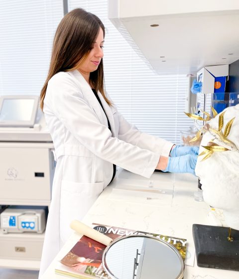 Angela Cusumano, PA-C, wearing gloves and preparing materials at a clinical workstation at Simply Dermatology.