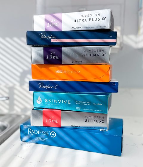 Stack of dermal fillers available at Simply Dermatology. Juvederm, Restylane, Radiesse, and Skinvive filler boxes stacked on each other. Prejuvenation treatments at Simply Dermatology.