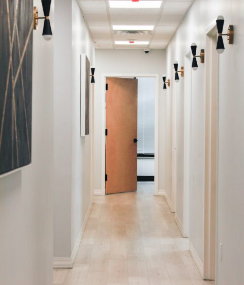A bright hallway inside Simply Dermatology featuring treatment room doors and modern wall lighting, creating a calm clinical environment.
