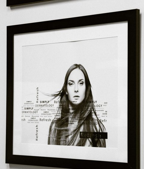 A framed black-and-white portrait of a woman displayed on the clinic wall at Simply Derm, featuring subtle text overlays with the Simply Dermatology branding.